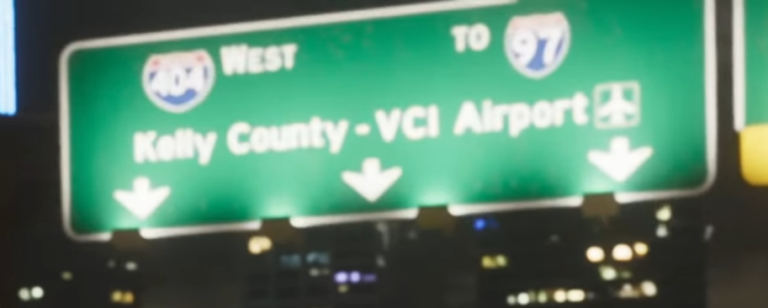 Дорожный указатель на зеленом фоне с надписями Kelly County - VCI Airport, направлениями на запад по трассе 40 и к трассе 97, а также символом аэропорта.