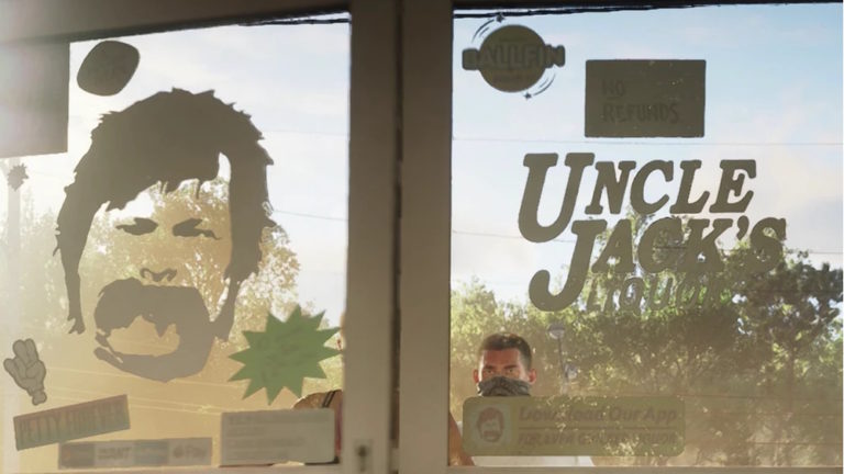 Вид изнутри магазина через стеклянную дверь с надписями Uncle Jack's Liquor, No Refunds и изображением лица с усами. За дверью стоит мужчина с повязкой на лице.