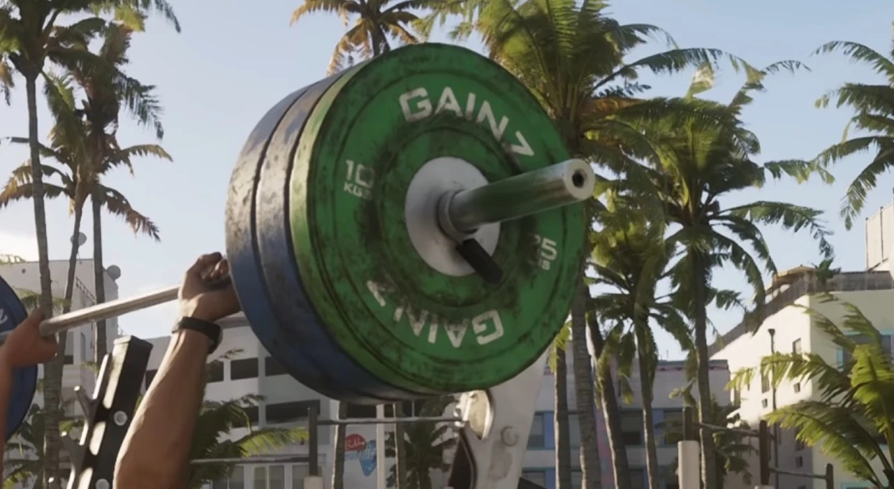 Штанга с зелёными и синими дисками GAINZ, 10 кг и 25 кг, поднята над головой на фоне пальм и городских зданий, солнечный день.