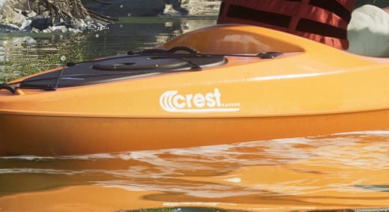 Оранжевый каяк с надписью crest на борту находится на спокойной воде, рядом видны отражения и часть человека в спасательном жилете.