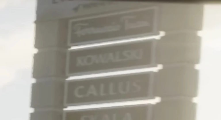Фрагмент вывески с фамилиями на здании: KOWALSKI, CALLUS, SKALA. Надписи выполнены белыми буквами на тёмном фоне, часть текста размыта.