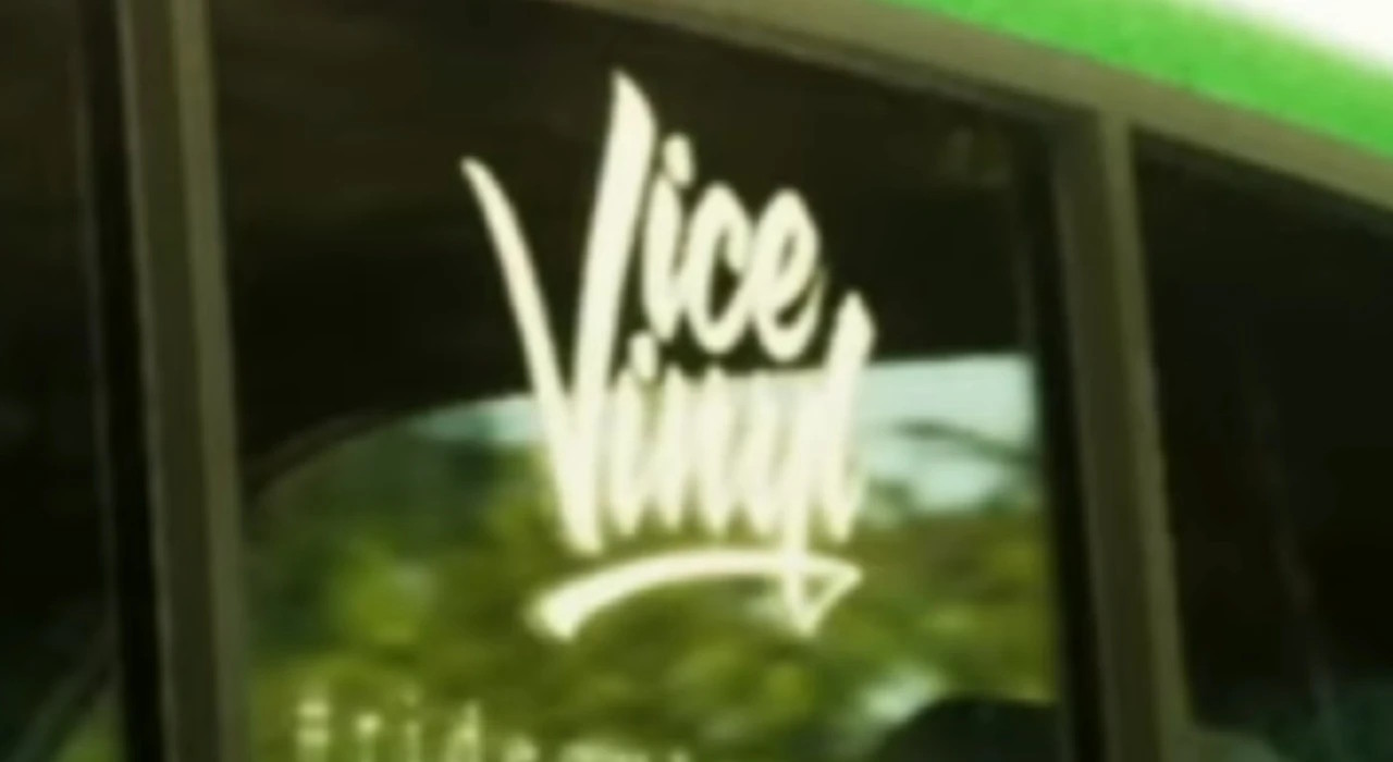 Наклейка с надписью Vice Vinyl на стекле автомобиля, выполненная белым цветом в стиле рукописного шрифта. На заднем плане видны размытые зелёные деревья и отражение окружающей среды. Окно автомобиля частично открыто, в верхней части заметна зелёная полоса. Надпись хорошо выделяется на тёмном фоне стекла, создавая контраст и привлекая внимание к бренду Vice Vinyl.