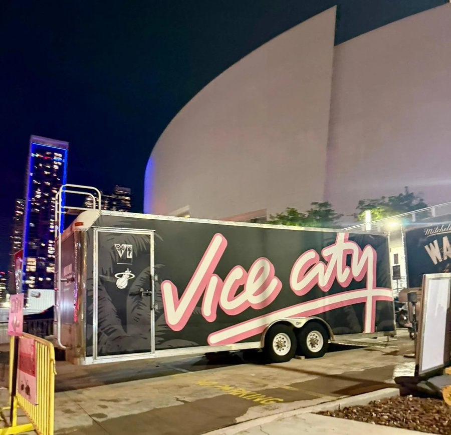 Трейлер с надписью Vice City и логотипом Miami Heat, припаркованный ночью на фоне современных зданий и неоновых огней. Ключевая фраза: Vice City.